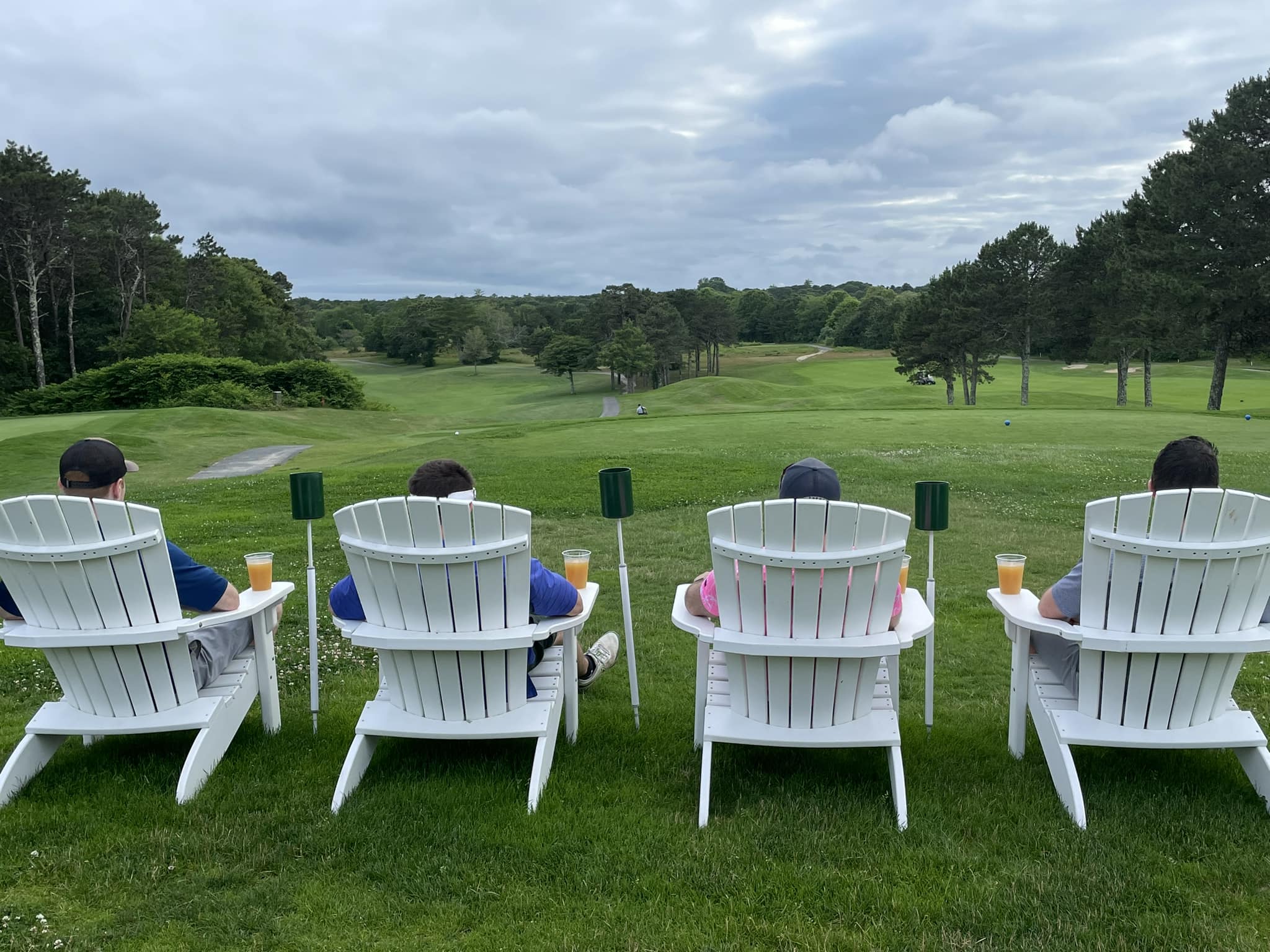 Guests relaxing in Adirondack chairs with drinks overlooking the green