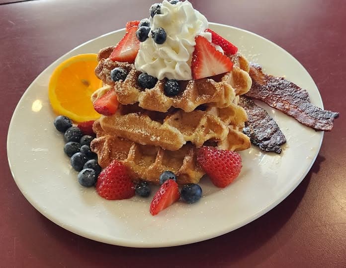 Belgian waffles stacked with fresh berries, whipped cream, and bacon